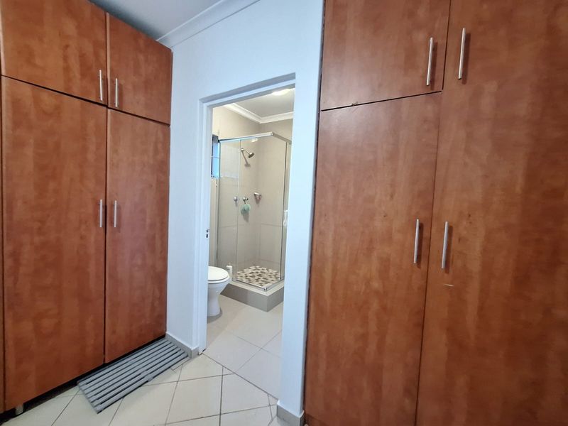 Bedroom featuring extensive built-in wooden cupboards and direct access to an en-suite bathroom with a glass-enclosed shower and tiled finishes.