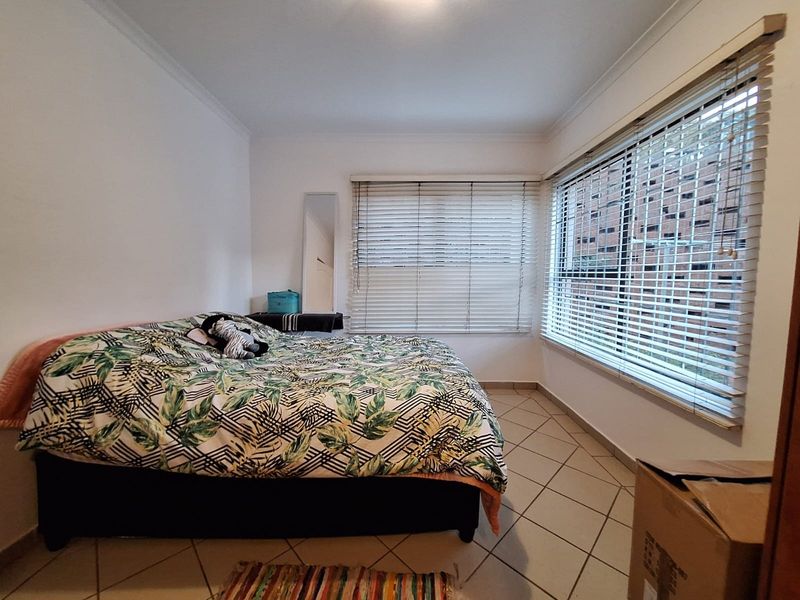 A bedroom featuring tiled flooring, neutral walls, and venetian blinds on the windows, providing a functional and well-lit living space.