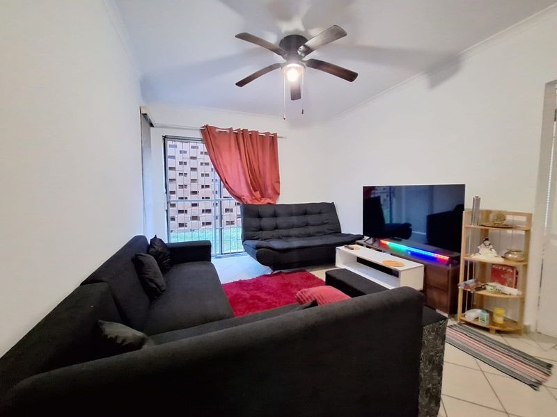 A living room featuring tiled flooring, a ceiling fan, and a sliding glass door providing access to the exterior.