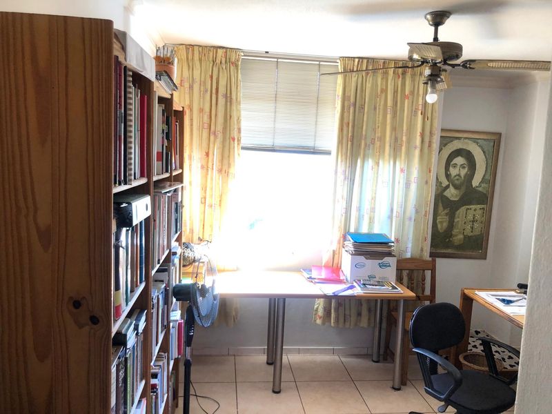 A functional home office space featuring tiled flooring, a ceiling fan, and a window with venetian blinds.