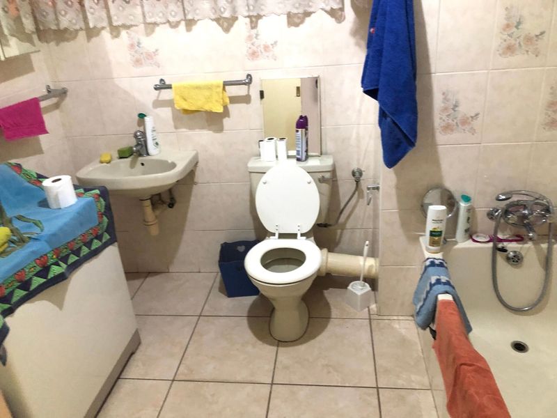 A dated bathroom featuring a wall-mounted basin, toilet, and bathtub with tiled finishes, requiring modernization of fixtures and plumbing concealment.