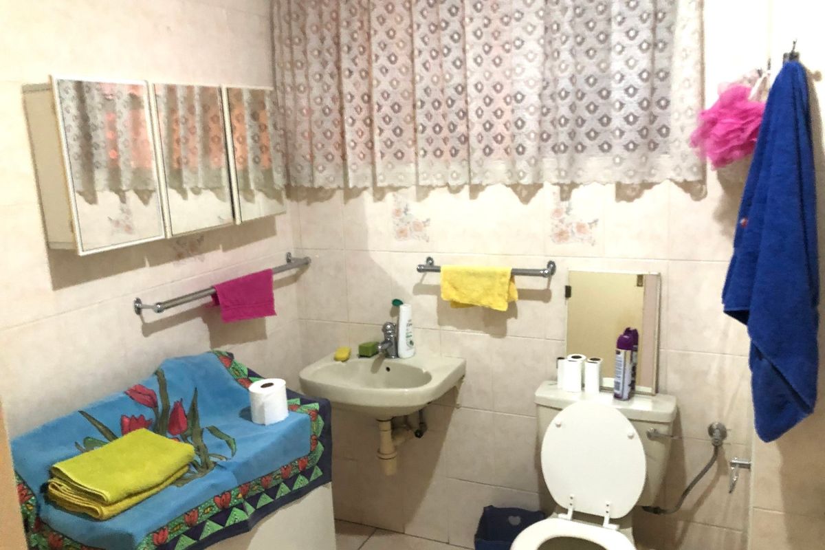 A functional bathroom featuring tiled walls and flooring, a wall-mounted basin, and a standard toilet.