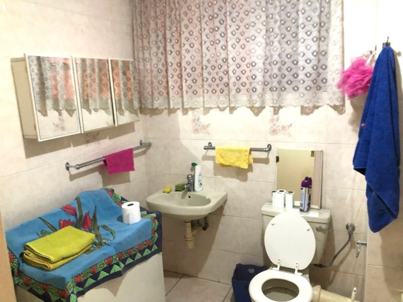 A functional bathroom featuring tiled walls and flooring, a wall-mounted basin, and a standard toilet.
