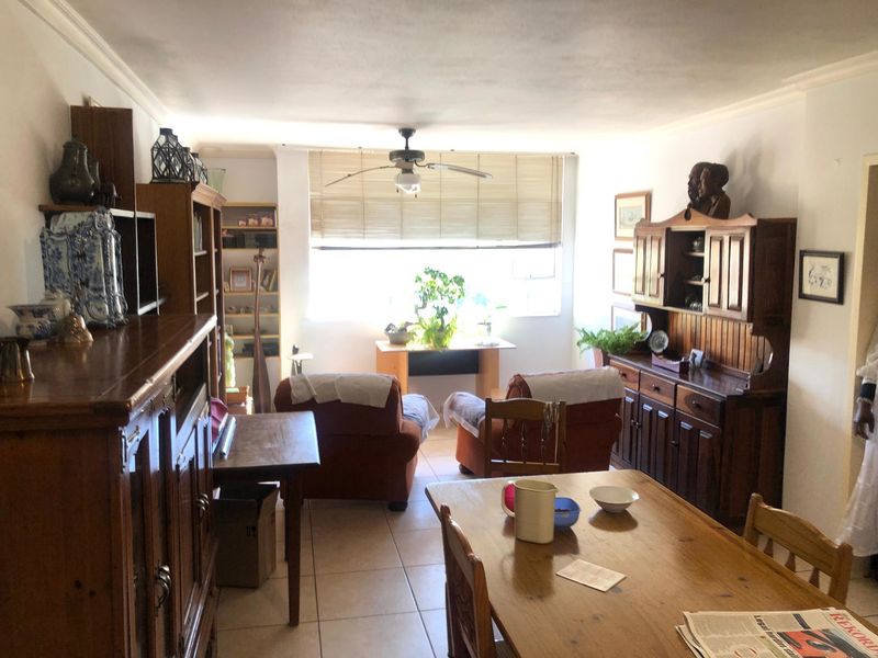 Open-plan living and dining area featuring tiled flooring, coved cornicing, and a ceiling fan, with natural light provided by a large window.