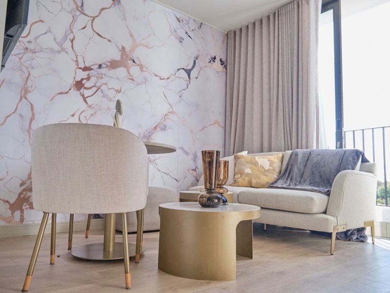 A modern living area featuring light laminate flooring, a striking marble-effect feature wall, and large sliding glass doors leading to a balcony.
