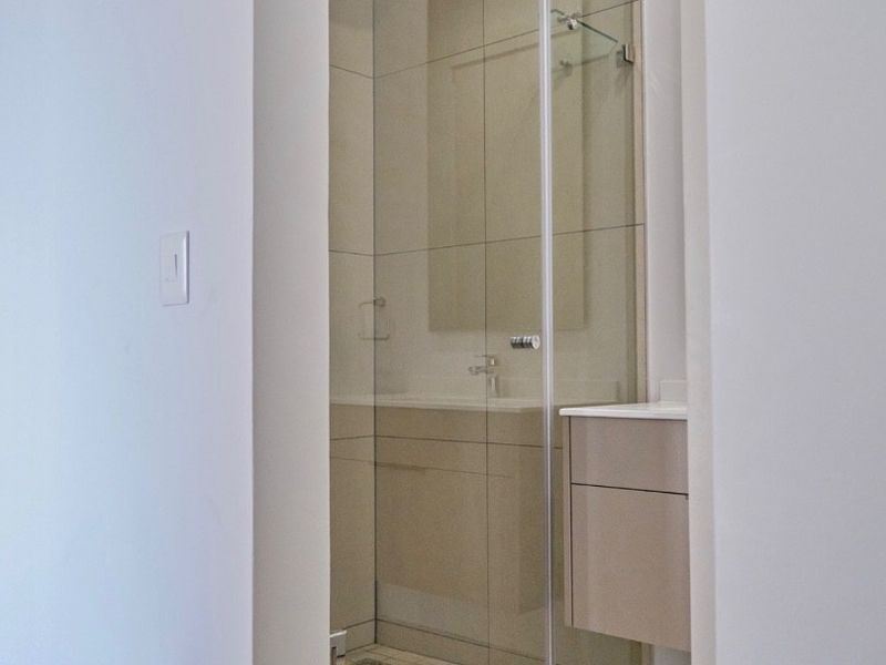 A modern, clean bathroom featuring a glass-enclosed shower with a rain shower head and a sleek wall-mounted vanity unit.