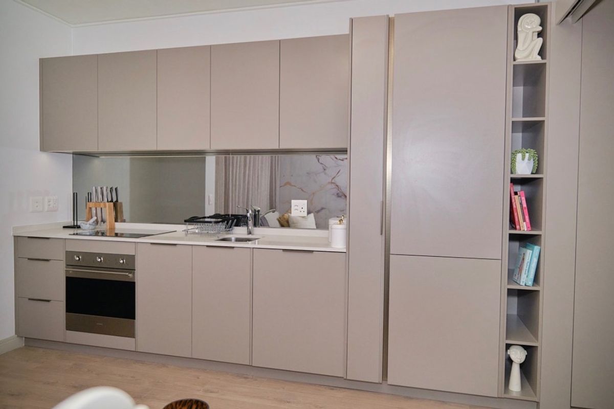 Modern kitchen featuring sleek taupe cabinetry, integrated oven, electric cooktop, stone countertops, and a reflective mirror splashback.