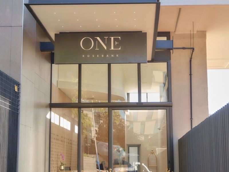Modern building entrance featuring a glass facade, prominent signage, and recessed lighting, providing a clean and professional aesthetic for the apartment complex.