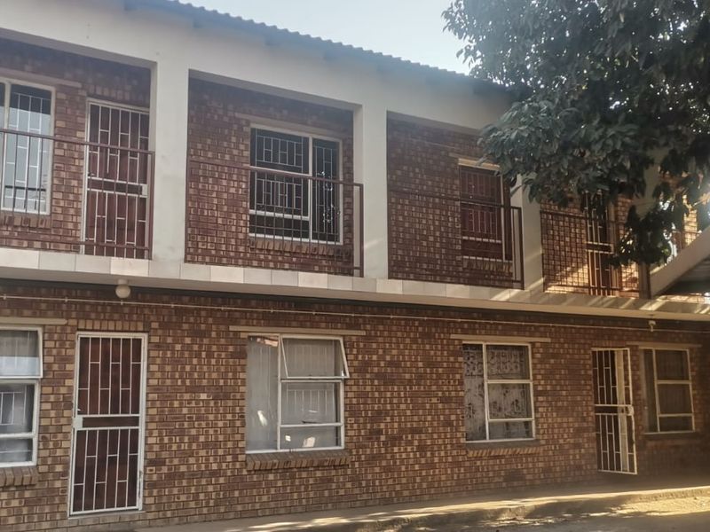 A two-story apartment building featuring a face brick facade, security gates, and balcony access on the upper level.