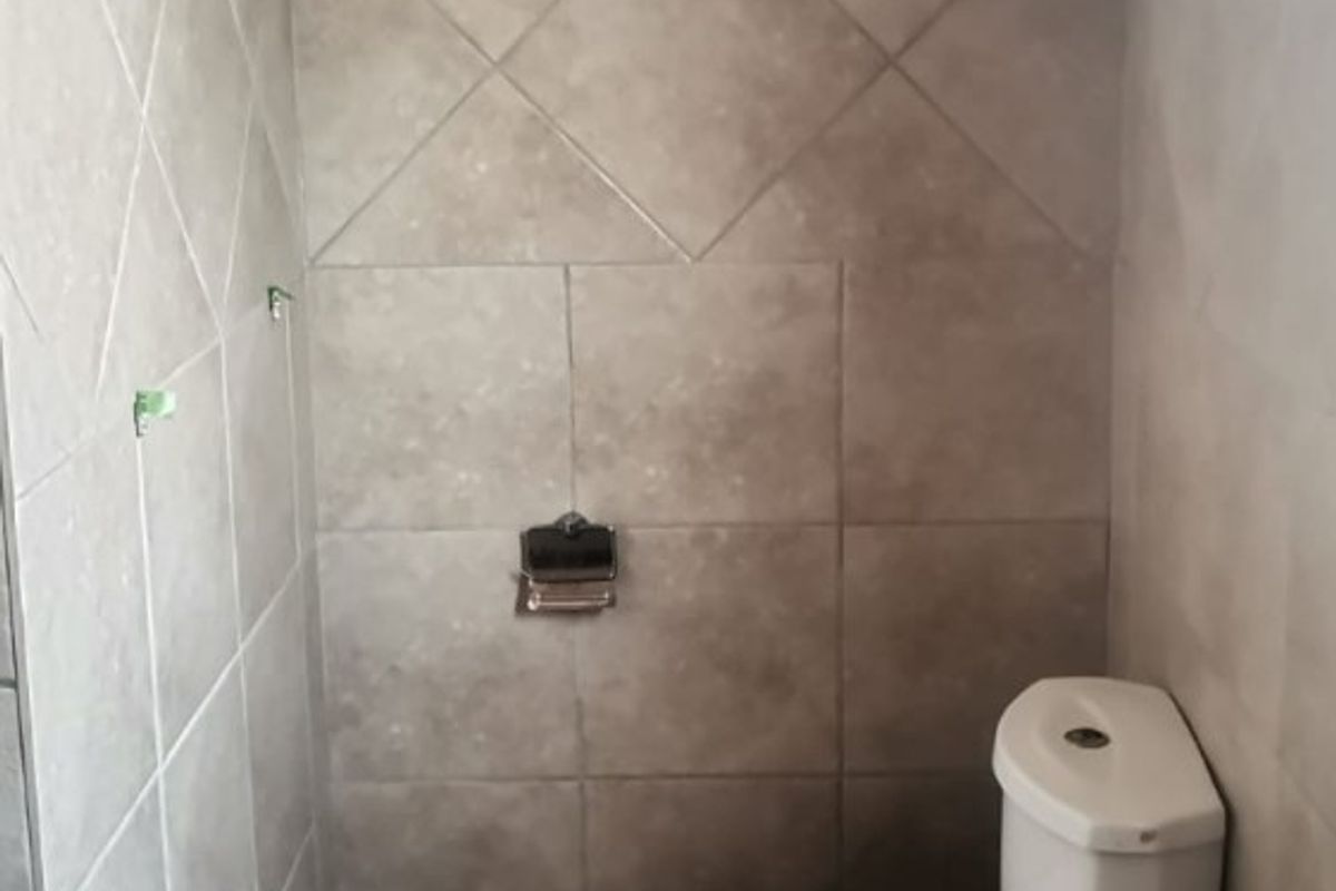 A compact bathroom featuring neutral ceramic wall and floor tiles, a standard white toilet, and a pedestal basin.
