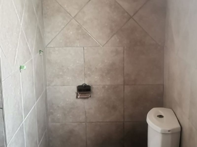 A compact bathroom featuring neutral ceramic wall and floor tiles, a standard white toilet, and a pedestal basin.
