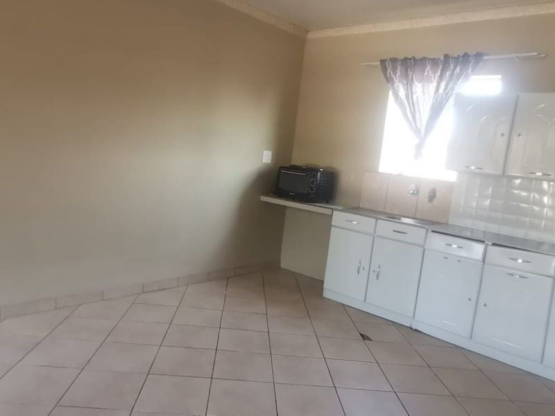 A functional kitchen area featuring white built-in cabinetry, tiled backsplash, and tiled flooring, offering a clean and simple layout ready for personalization.