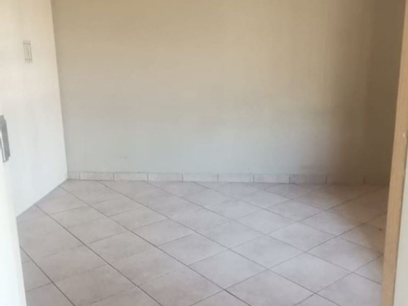 An empty bedroom featuring neutral tiled flooring and a built-in cupboard, offering a blank canvas for personalization.