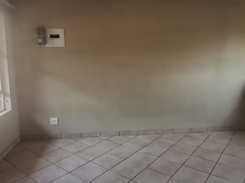An empty living area featuring tiled flooring, security bars on the window, and a built-in wall shelf, ready for personalization.