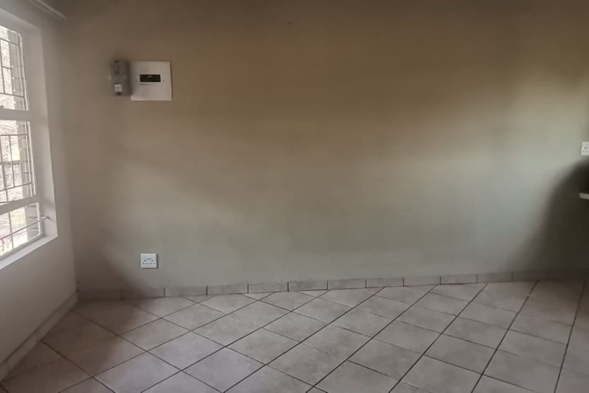 An empty living area featuring tiled flooring, security bars on the window, and a built-in wall shelf, ready for personalization.
