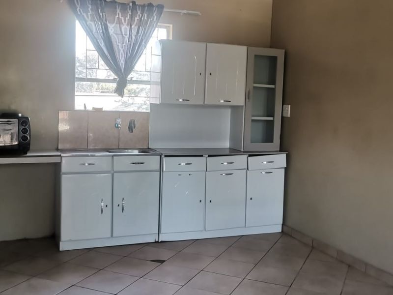 A functional kitchen area featuring built-in white cabinetry, a stainless steel sink, tiled splashback, and ceramic floor tiles.