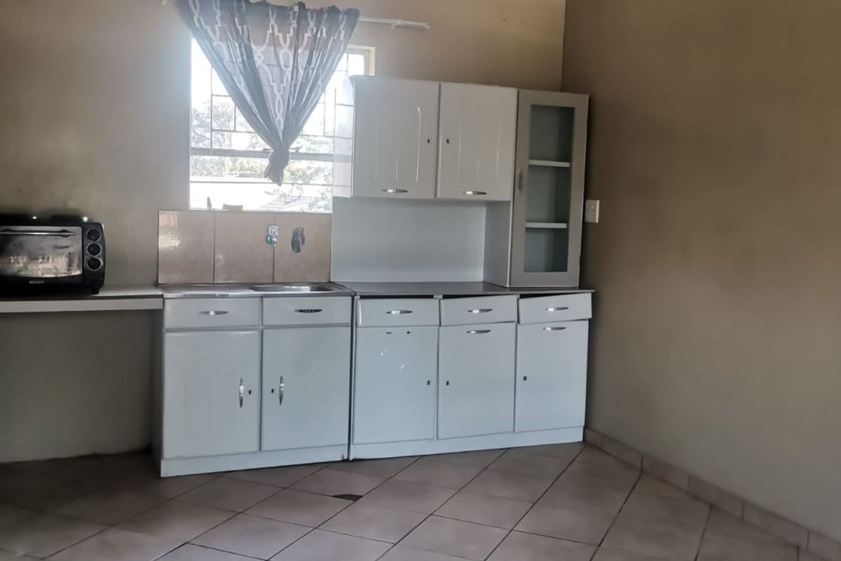 A functional kitchen area featuring built-in white cabinetry, a stainless steel sink, tiled splashback, and ceramic floor tiles.