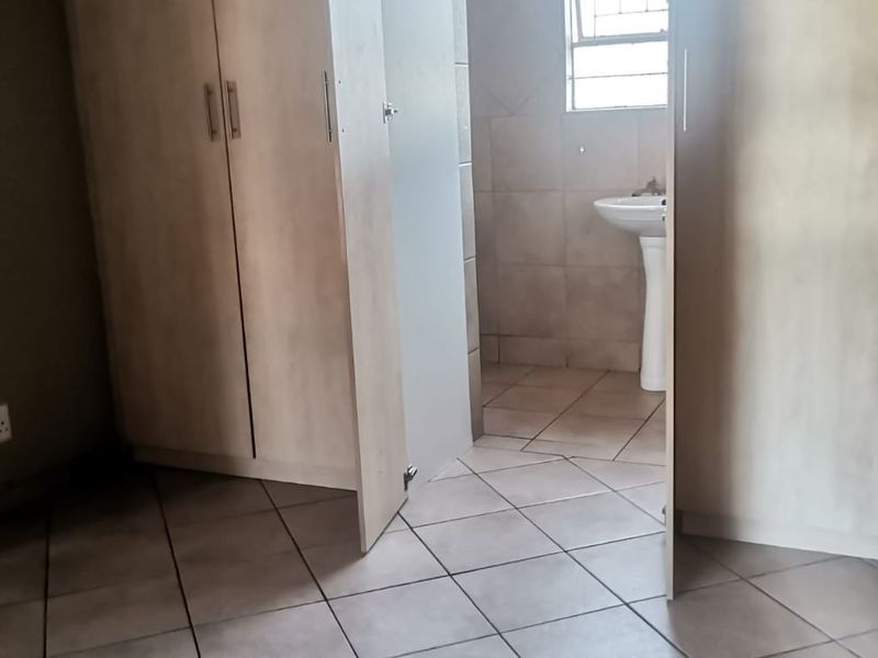 A bedroom featuring built-in cupboards and tiled flooring, with an adjoining en-suite bathroom area containing a pedestal basin.