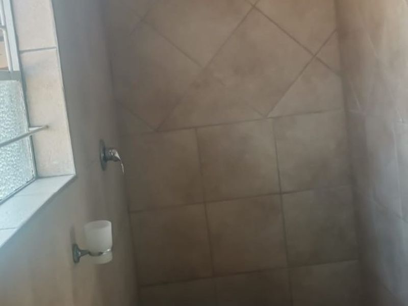 A compact bathroom featuring a pedestal washbasin and a tiled shower enclosure with a shower head.