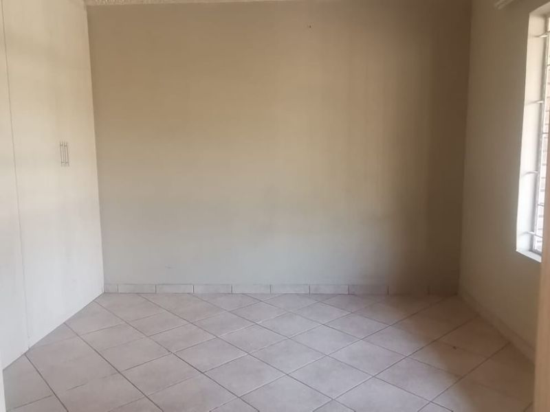 An empty bedroom featuring tiled flooring, built-in cupboards, and a window with security bars, offering a blank canvas for personalization.