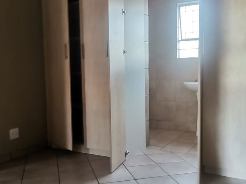 A bedroom featuring built-in cupboards and tiled flooring, with an adjoining en-suite bathroom area containing a pedestal basin.