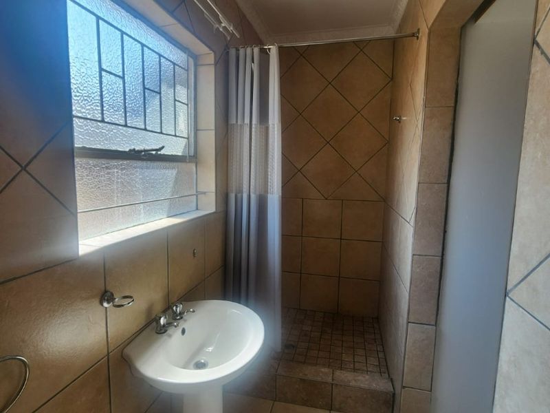 A functional bathroom featuring a pedestal basin, tiled walls and flooring, and a shower cubicle with a curtain rail.