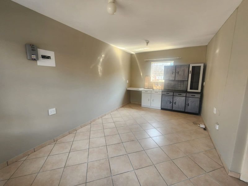 An empty kitchen area featuring tiled flooring, basic cabinetry with a sink, and a wall-mounted electrical distribution board.