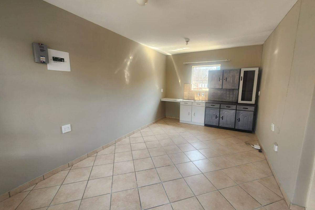 An empty kitchen area featuring tiled flooring, basic cabinetry with a sink, and a wall-mounted electrical distribution board.