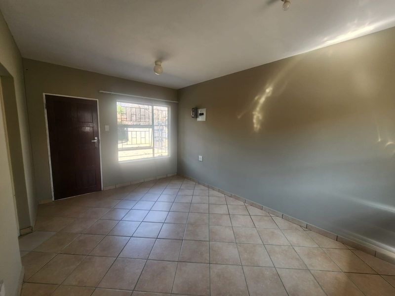 An empty living room featuring neutral wall paint, tiled flooring, and a window with security bars.