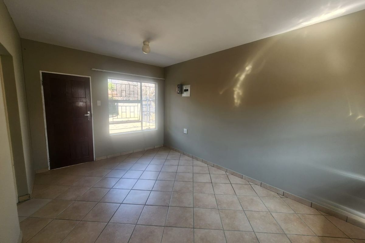 An empty living room featuring neutral wall paint, tiled flooring, and a window with security bars.