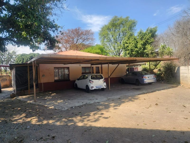 Rear exterior view of the property featuring a large carport structure, concrete driveway, and perimeter walling.