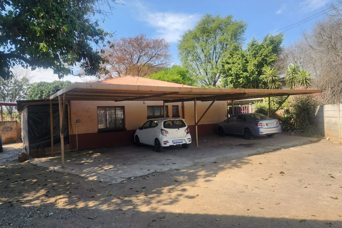 Rear exterior view of the property featuring a large carport structure, concrete driveway, and perimeter walling.