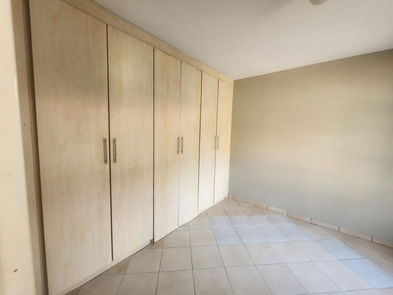 A clean, empty bedroom featuring neutral tiled flooring and extensive built-in wooden cupboards providing ample storage space.