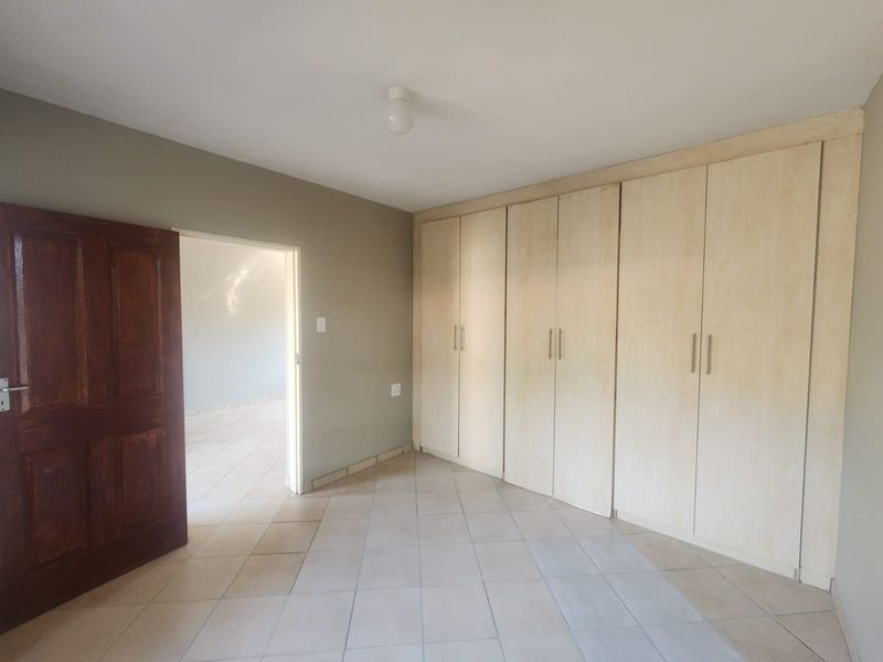A spacious, empty bedroom featuring neutral wall tones, tiled flooring, and extensive built-in cupboard storage.