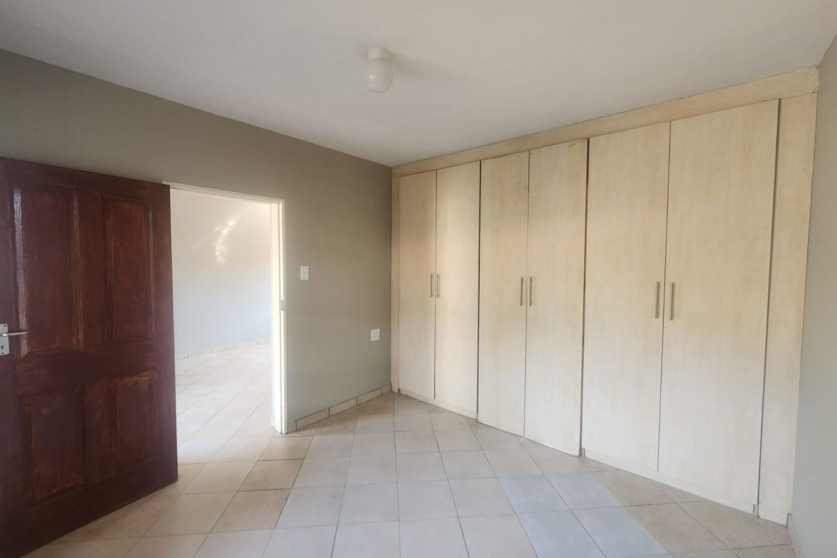 A spacious, empty bedroom featuring neutral wall tones, tiled flooring, and extensive built-in cupboard storage.