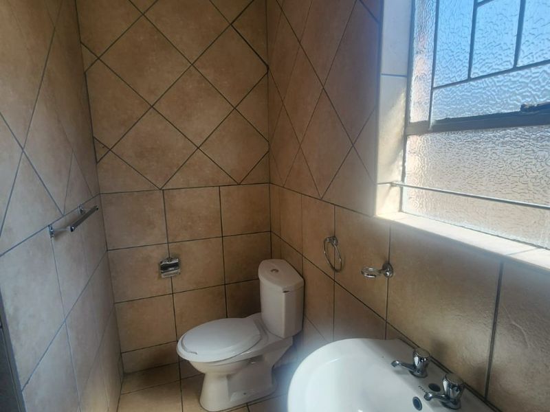 A compact bathroom featuring floor-to-ceiling tiled walls, a pedestal basin, and a toilet, illuminated by a large obscured glass window.