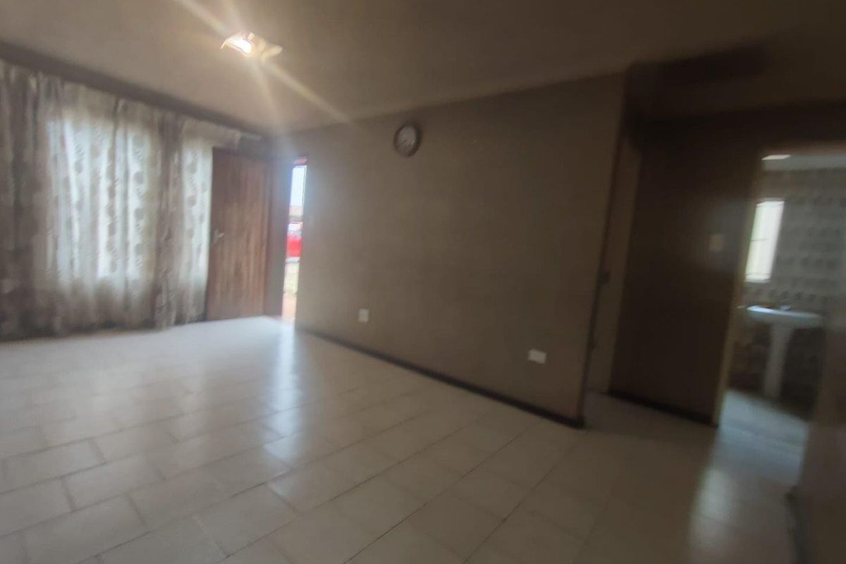 An empty living room featuring tiled flooring and neutral wall finishes, with an adjacent view into a bathroom area.