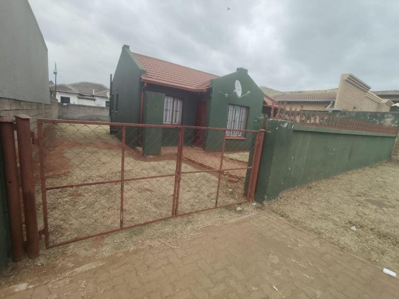 Front view of a detached house featuring a tiled roof, perimeter wall with metal gate, and security bars on windows.