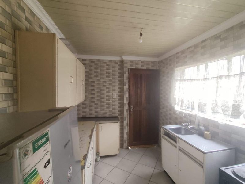 A functional kitchen featuring built-in cabinetry, tiled splashbacks, and a stainless steel sink, offering potential for modernization and cosmetic updates.