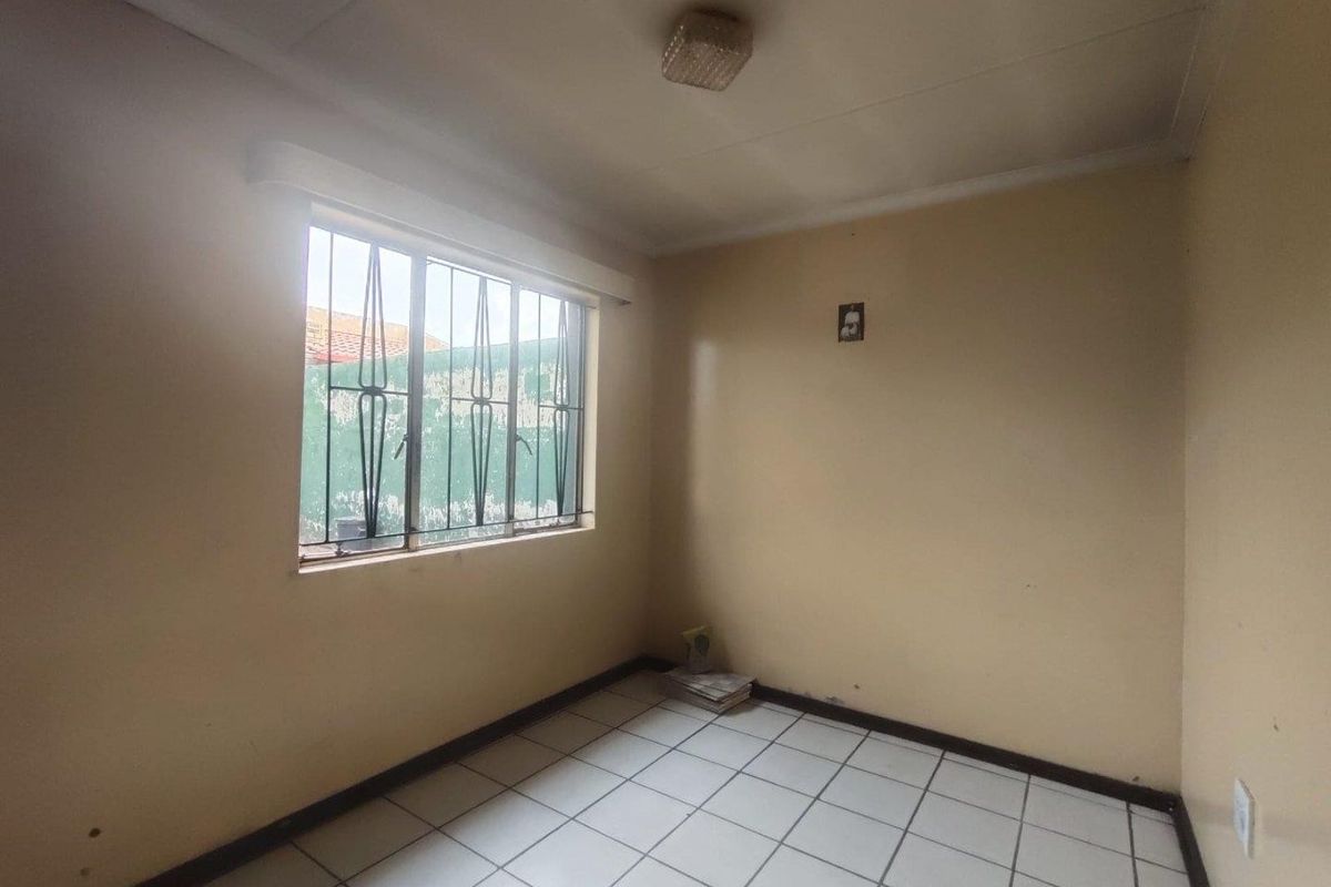 An empty bedroom featuring tiled flooring, a ceiling light fixture, and a window fitted with security bars.