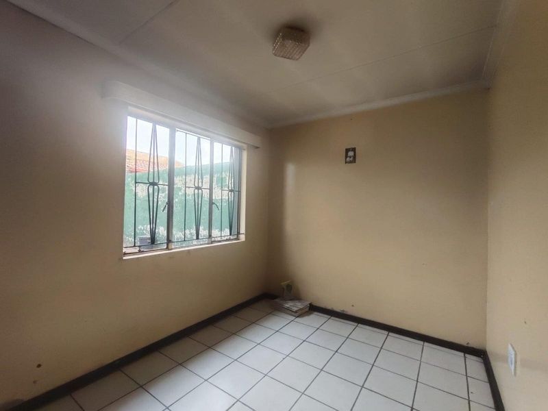 An empty bedroom featuring tiled flooring, a ceiling light fixture, and a window fitted with security bars.