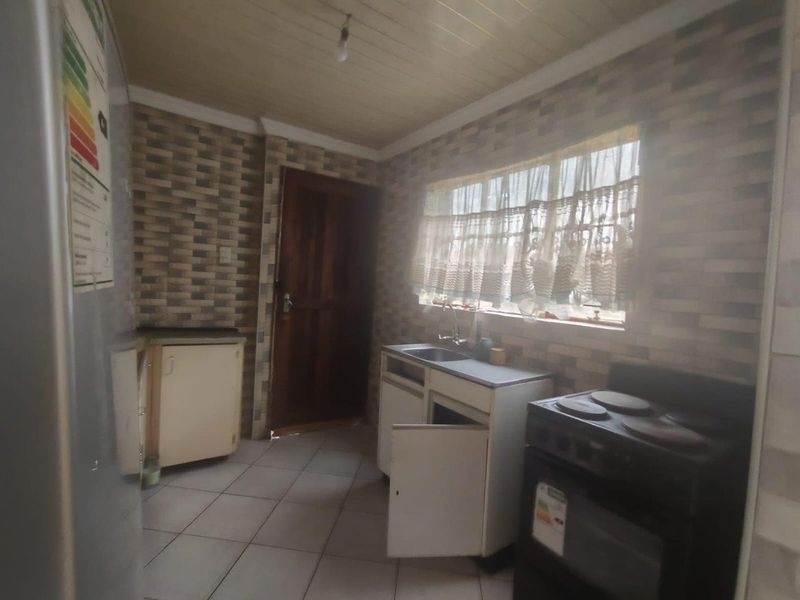A dated kitchen featuring tiled flooring, timber ceiling, and basic cabinetry. The space requires modernization to improve functionality and aesthetic appeal.