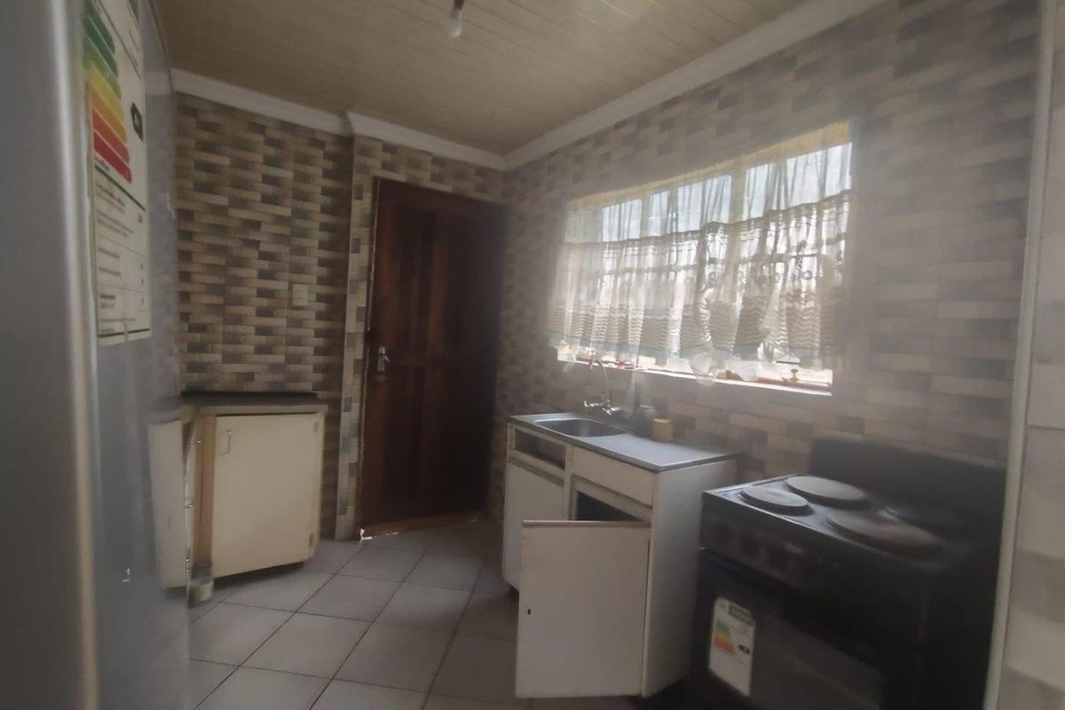 A dated kitchen featuring tiled flooring, timber ceiling, and basic cabinetry. The space requires modernization to improve functionality and aesthetic appeal.
