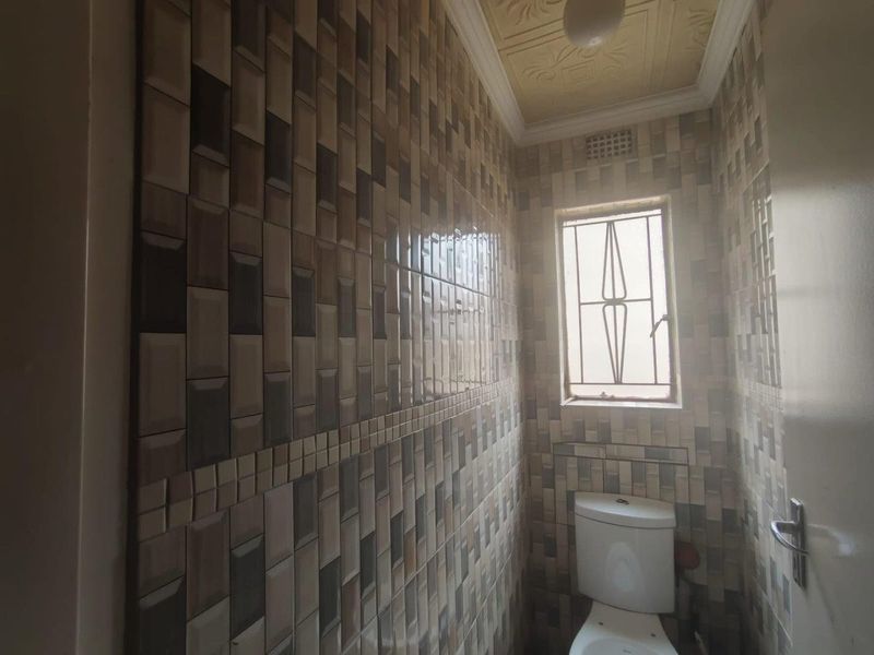 A compact bathroom featuring full-height decorative wall tiling, a standard toilet, and a window with security bars.