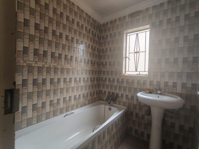 A functional bathroom featuring a pedestal basin, bathtub, and full-height wall tiling with a window for natural light.