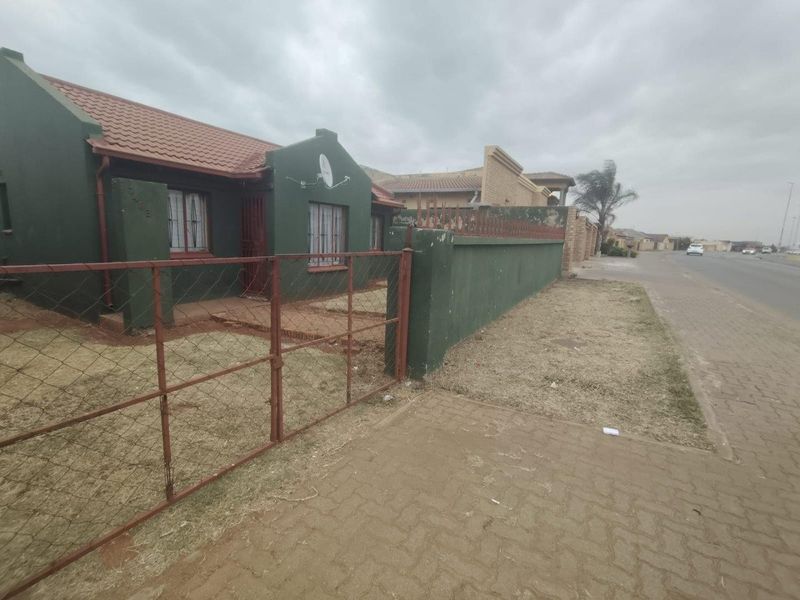 Front exterior view of a single-story house featuring a tiled roof, perimeter wall, and metal gate access.