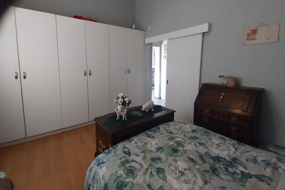 A well-maintained bedroom featuring extensive built-in cupboard storage, laminate flooring, and a functional sliding door leading to the hallway.