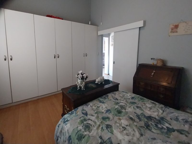 A well-maintained bedroom featuring extensive built-in cupboard storage, laminate flooring, and a functional sliding door leading to the hallway.