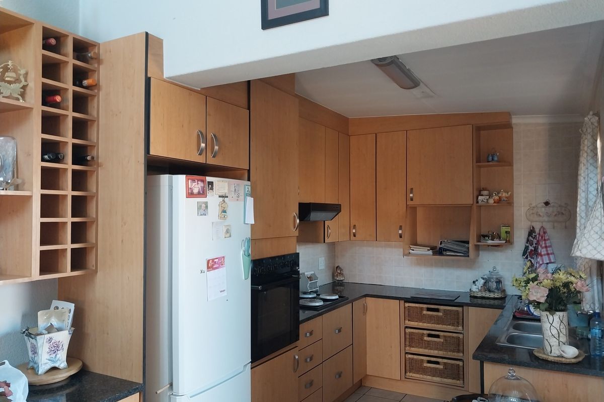 A functional kitchen featuring light wood cabinetry, laminate countertops, built-in oven, hob, and a double bowl sink with tiled flooring.