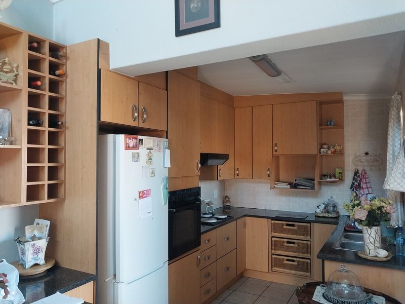 A functional kitchen featuring light wood cabinetry, laminate countertops, built-in oven, hob, and a double bowl sink with tiled flooring.
